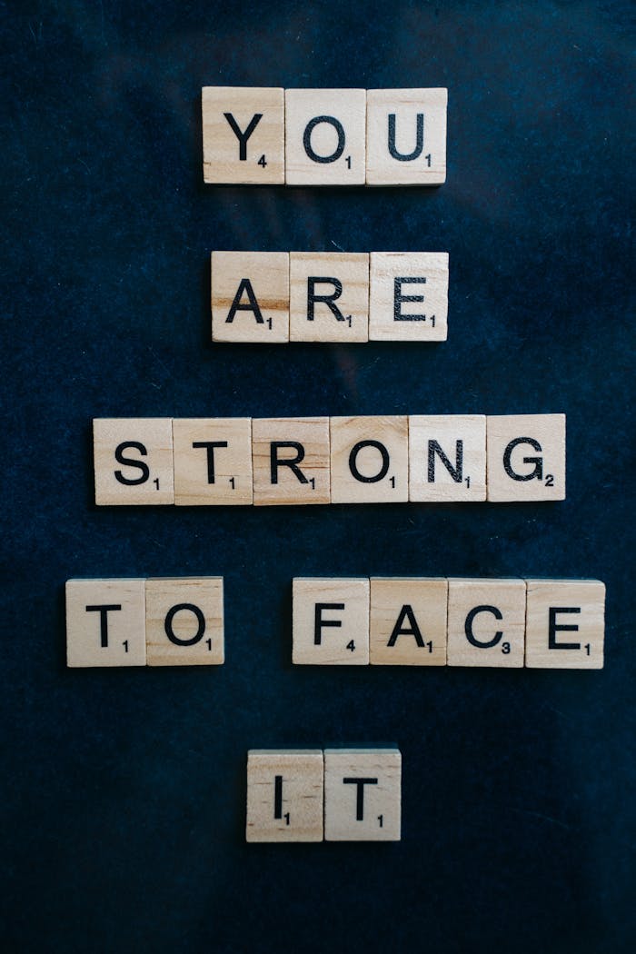 Wooden Scrabble tiles spell out You are strong to face it on a dark surface, conveying a motivational message.